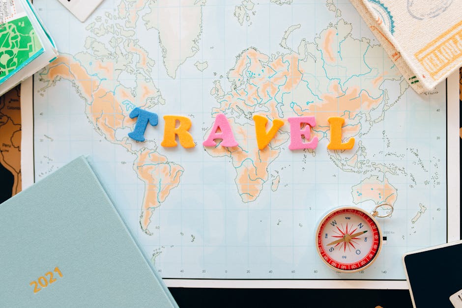 Flat lay of a map with colorful letters TRAVEL and a compass for planning adventures
